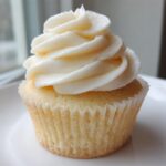 A single, perfectly baked vanilla cupcake with a tall swirl of white vanilla buttercream frosting.