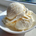 Close-up of several scoops of creamy, vanilla-colored protein ice cream served in a white bowl.