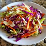 A close-up of a vibrant, crunchy cabbage salad featuring shredded red and green cabbage, carrots, and red onion.