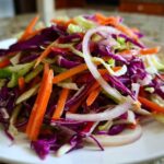 Close-up of a vibrant cabbage salad featuring shredded red cabbage, green cabbage, carrots, and sliced red onion.