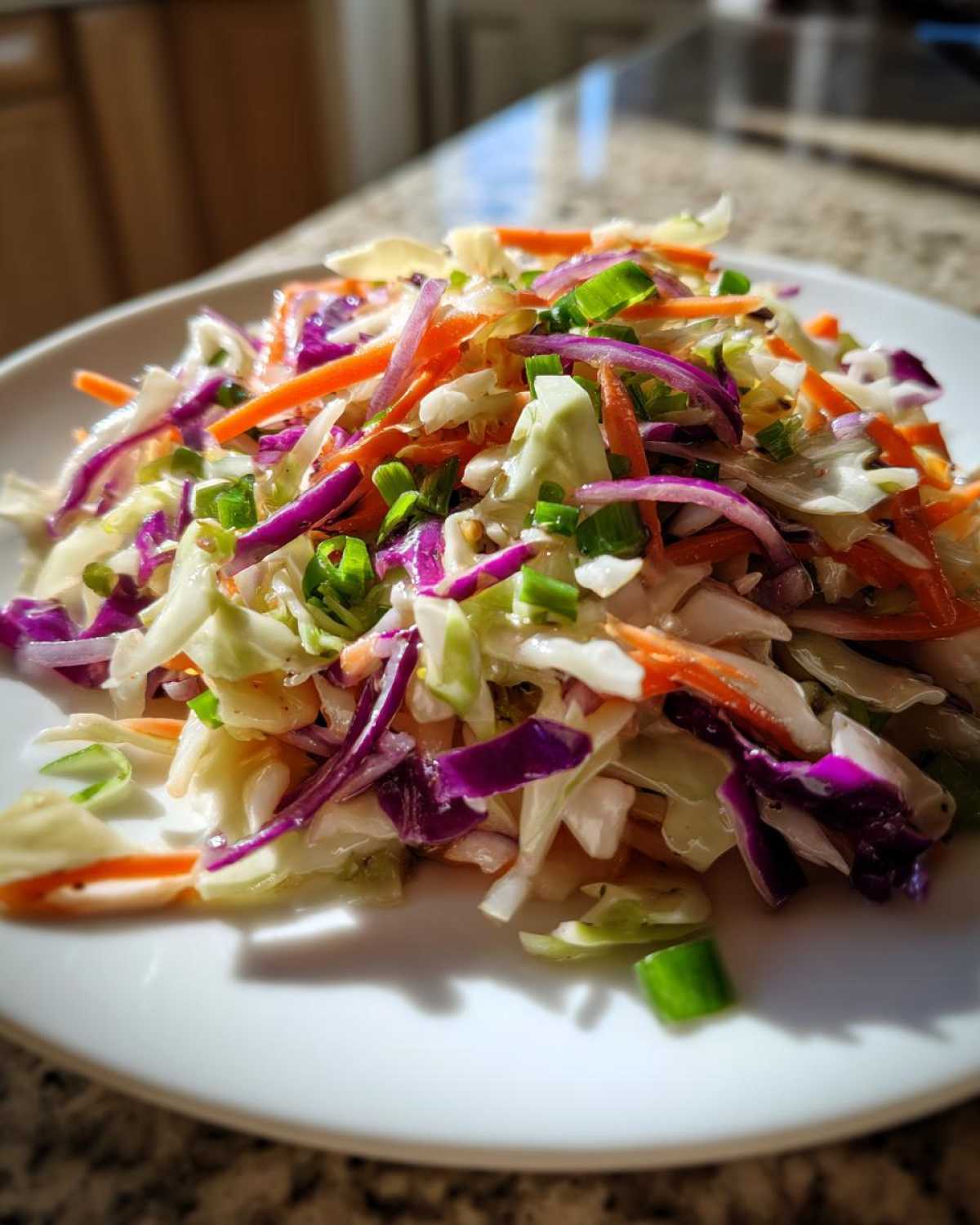 A close-up of a vibrant cabbage salad featuring shredded green and purple cabbage, carrots, and green onions on a white plate.
