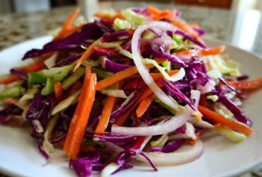 Close-up of a vibrant cabbage salad featuring shredded red cabbage, green cabbage, carrots, and sliced red onion.