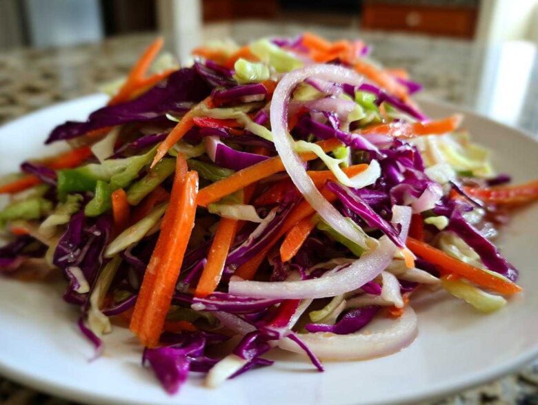 Close-up of a vibrant cabbage salad featuring shredded red cabbage, green cabbage, carrots, and sliced red onion.