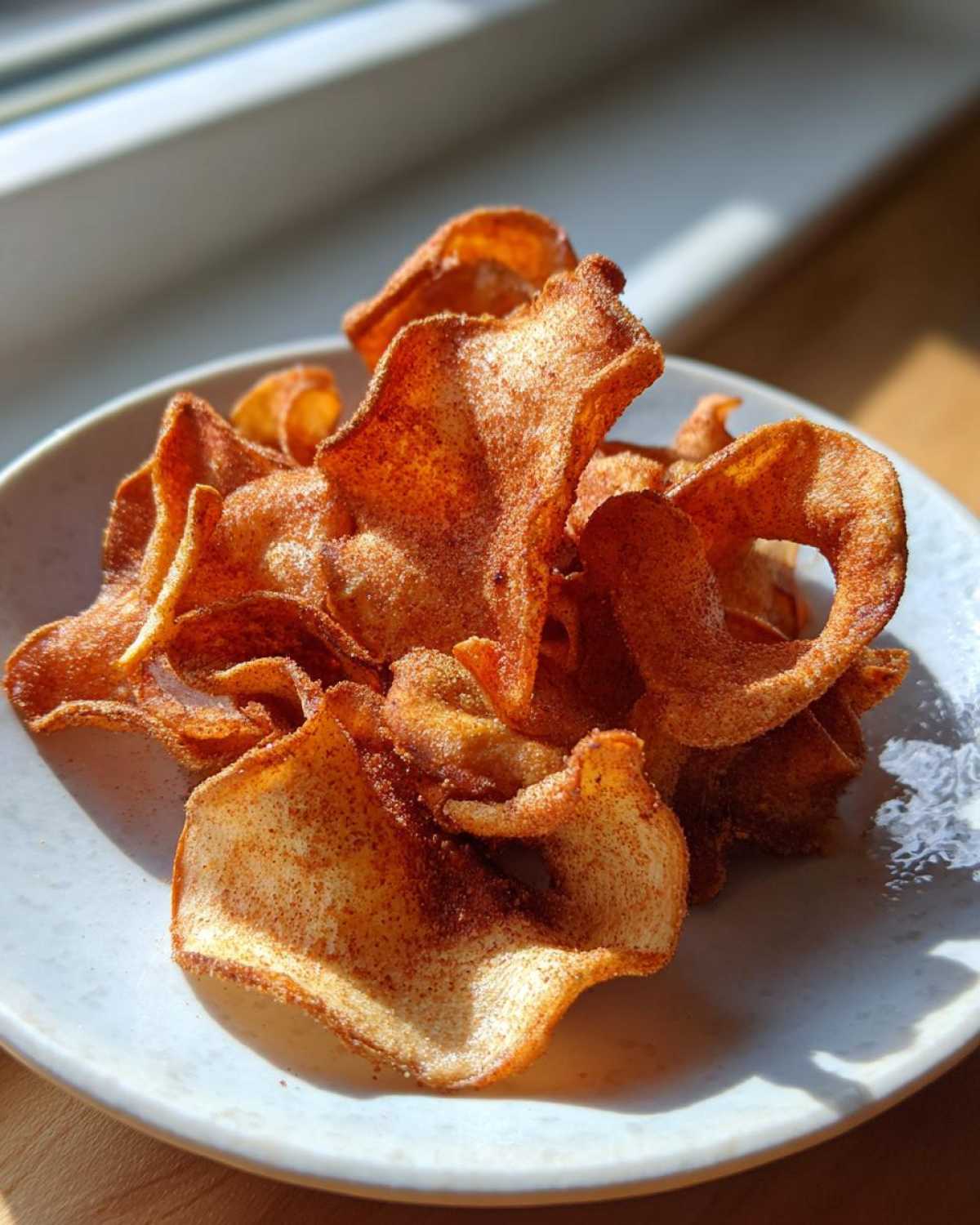 A pile of crispy Air Fryer Cinnamon Sugar Apple Chips dusted heavily with cinnamon on a light-colored plate.