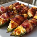 A platter of crispy, bacon-wrapped Air Fryer Stuffed Jalapeno Poppers filled with melted cheese.