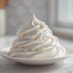 A tall, perfect swirl of thick, white Copycat Cinnabon Cream Cheese Frosting piped onto a small white saucer.