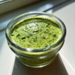 Close-up of vibrant green Copycat Panera Green Goddess Dressing with visible herb flecks in a small glass container.