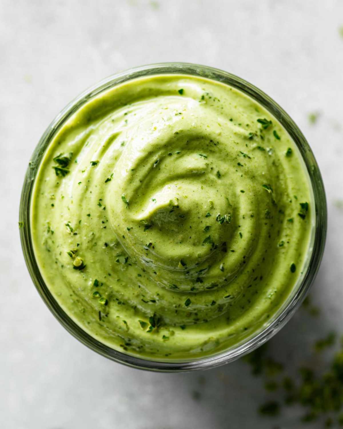 Overhead view of thick, bright green Copycat Panera Green Goddess Dressing swirled in a glass jar, topped with herbs.