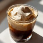 A glass of iced coffee topped with thick Copycat Starbucks Vanilla Sweet Cream Cold Foam, illuminated by sunlight.