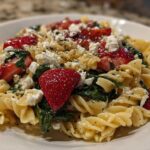 A close-up serving of Easy Strawberry Spinach Pasta Salad with Feta, featuring fusilli pasta, bright red strawberries, wilted spinach, and crumbled feta cheese.