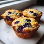 Three golden Gluten-Free Blueberry Lemon Muffin Tops topped with bright yellow lemon zest and bursting blueberries.