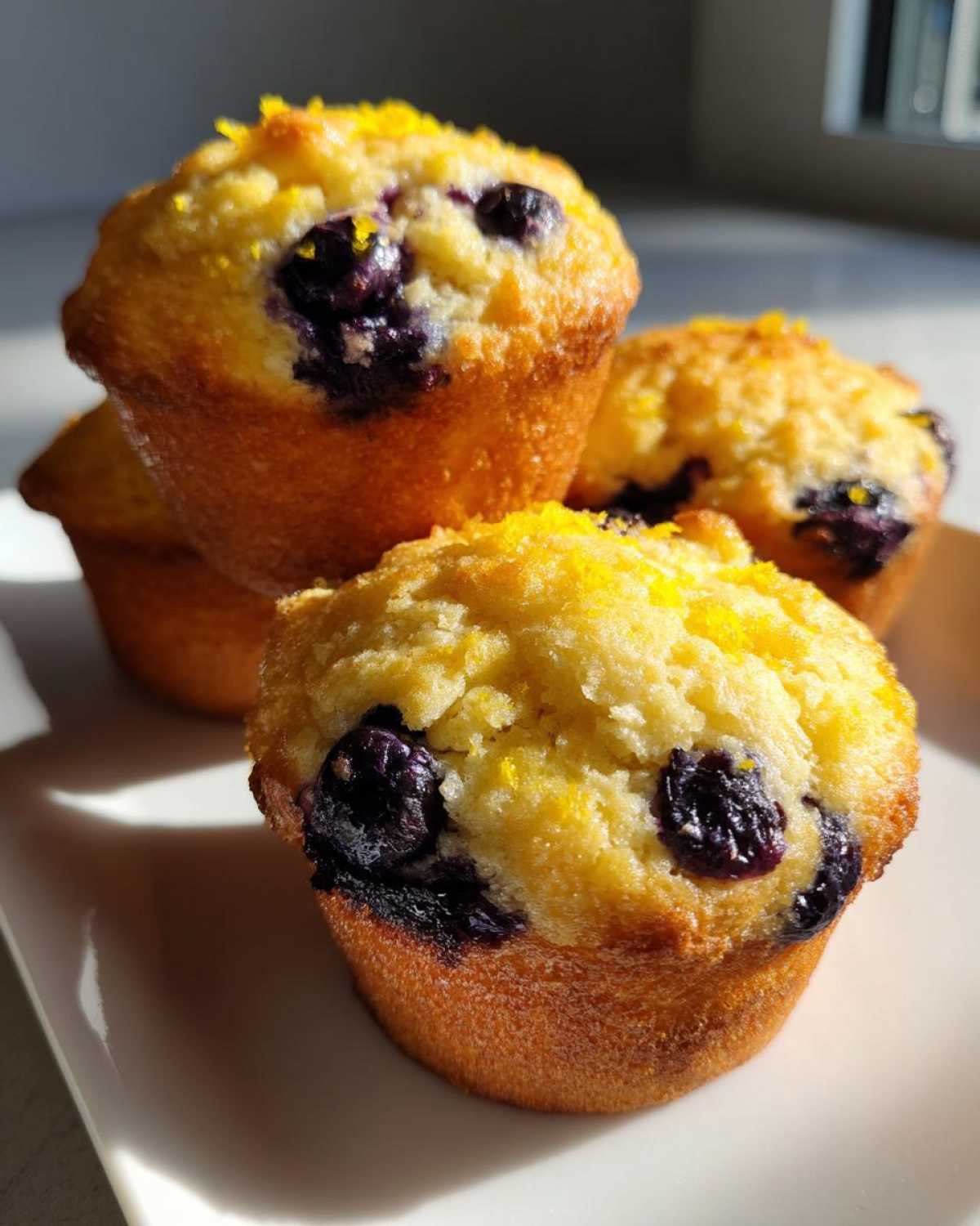 Close-up of golden Gluten-Free Blueberry Lemon Muffin Tops topped with bright yellow lemon zest.