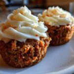 Close-up of two Gluten-Free Carrot Cake Cupcakes topped with thick swirls of cream cheese frosting.