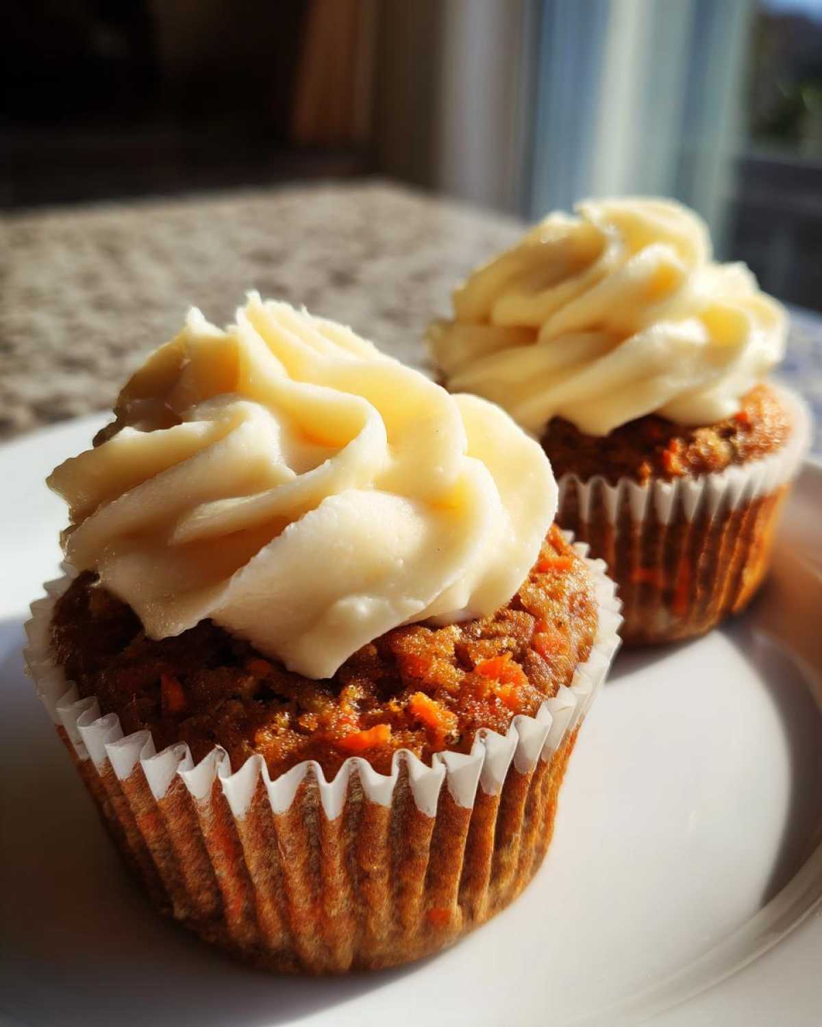 Two Gluten-Free Carrot Cake Cupcakes topped with thick swirls of cream cheese frosting on a white plate.