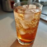 Close-up of a tall glass filled with bubbling Iced Peach Green Tea and large ice cubes.