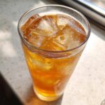 Close-up of a tall glass filled with cold Iced Peach Green Tea and condensation on the outside.