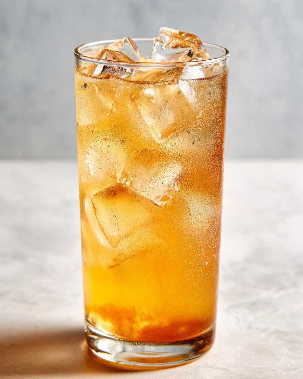 Close-up of a tall glass filled with condensation, ice cubes, and golden Iced Peach Green Tea.