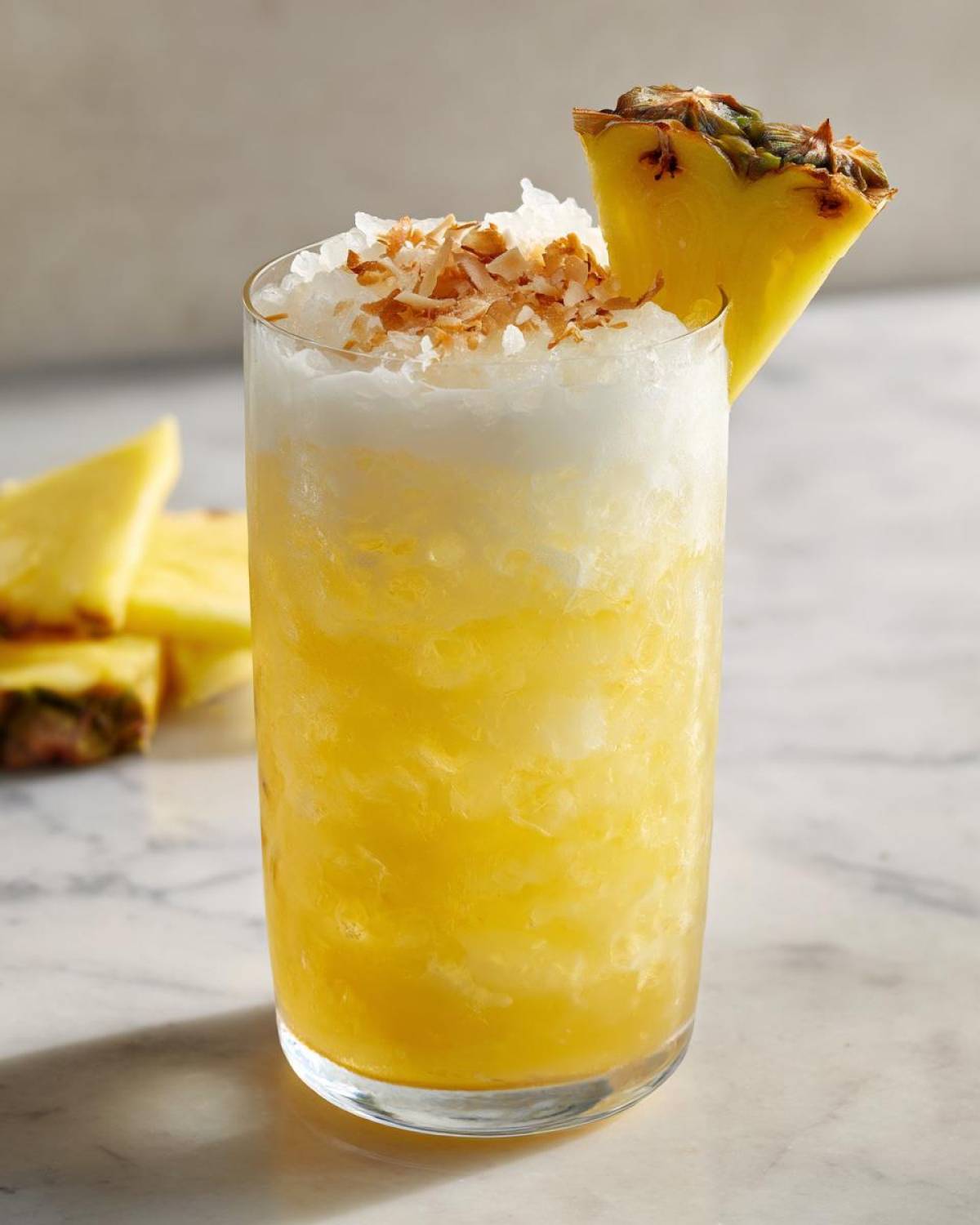 A tall glass of Iced Pineapple Coconut Mocktail topped with crushed ice and toasted coconut flakes.