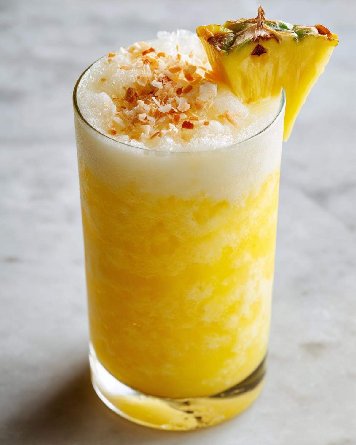 Close-up of a tall glass containing a vibrant Iced Pineapple Coconut Mocktail, topped with crushed ice and toasted coconut flakes.
