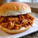A close-up of a juicy Instant Pot BBQ Pulled Chicken Sandwich served on a white plate.