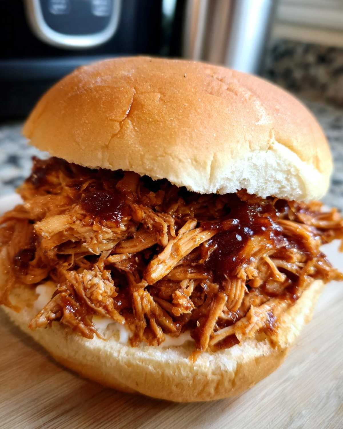 A close-up of a juicy Instant Pot BBQ Pulled Chicken Sandwich served on a soft bun with sauce.