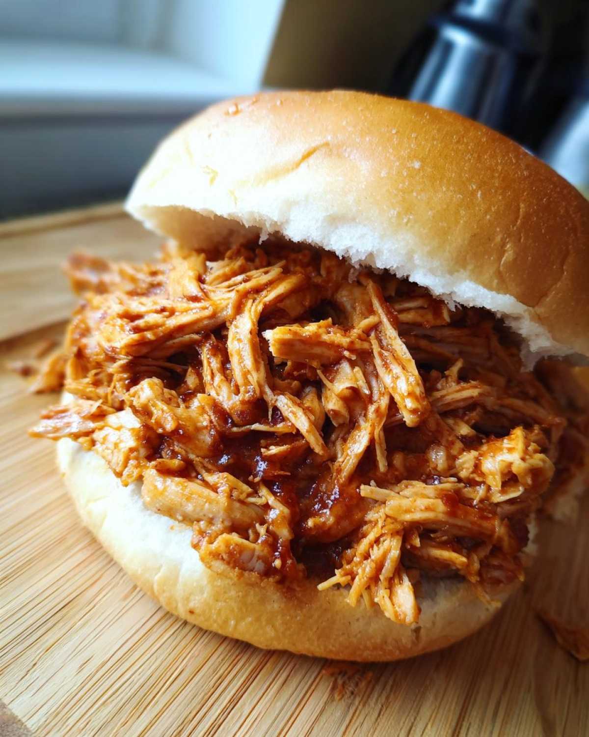 A close-up shot of a fluffy bun overflowing with saucy Instant Pot BBQ Pulled Chicken.