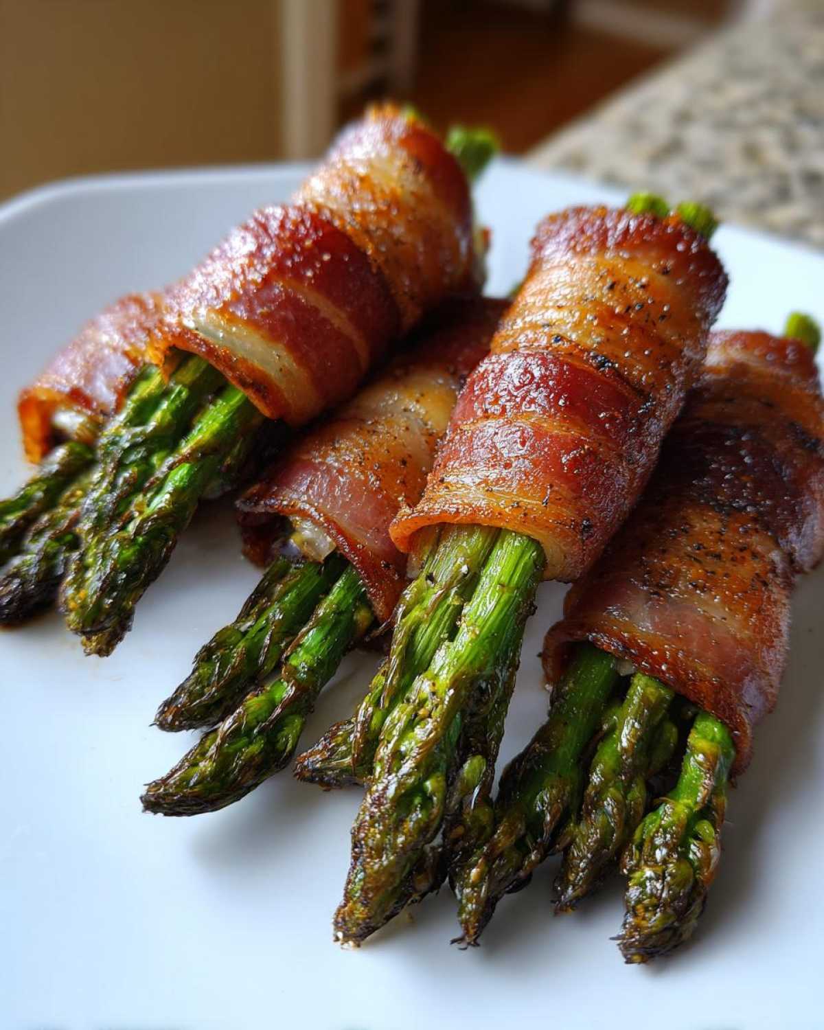 Close-up of perfectly cooked Keto Bacon Wrapped Asparagus Bundles seasoned with pepper on a white plate.