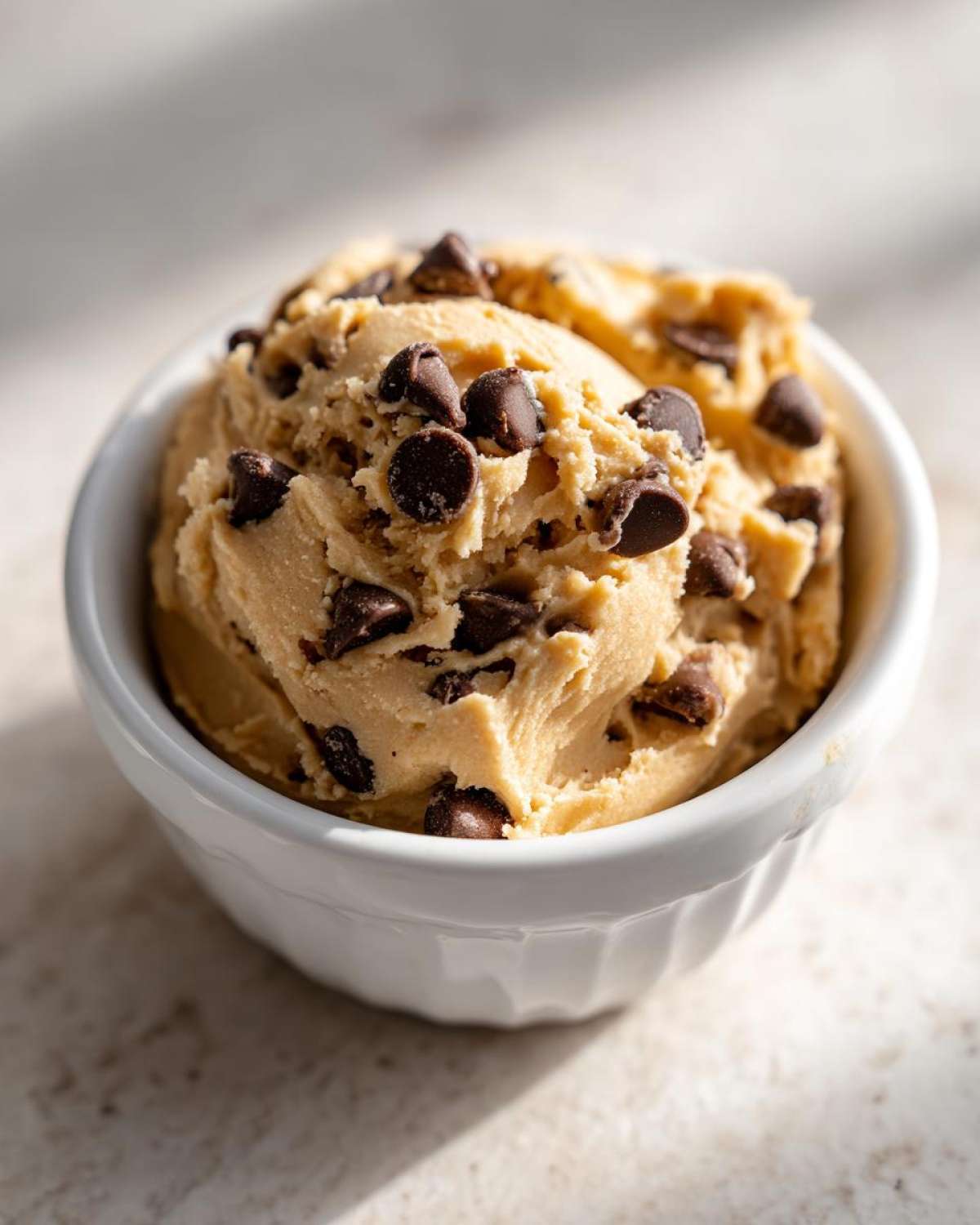 A close-up of a white bowl filled with thick, creamy Keto Chocolate Chip Cookie Dough Dip loaded with mini chocolate chips.