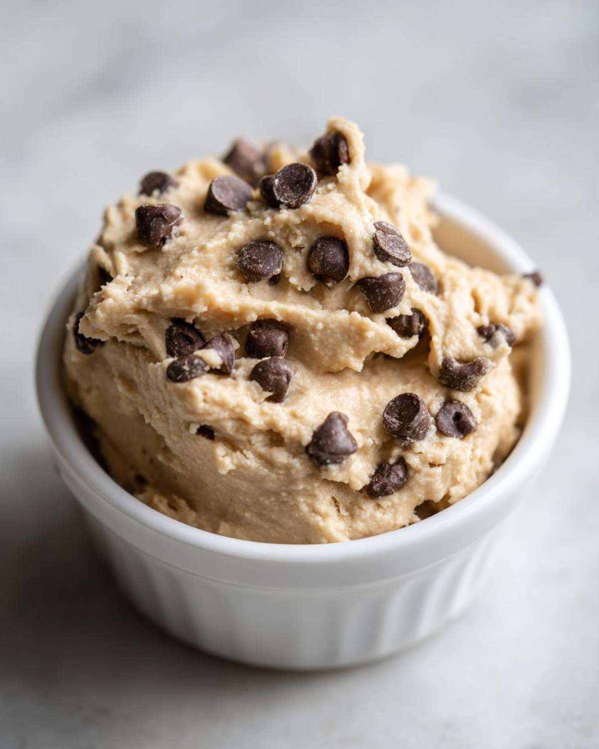 Close-up of a small white ramekin filled with thick Keto Chocolate Chip Cookie Dough Dip topped with mini chocolate chips.