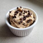 A small white ramekin filled with thick Keto Chocolate Chip Cookie Dough Dip topped generously with mini chocolate chips.