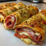 Close-up of three baked Keto Italian Sub Roll-Ups showing melted cheese, pepperoni, and salami filling.