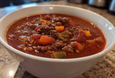 Close-up of a steaming white bowl filled with rich, red Keto Taco Soup with Ground Beef and diced vegetables.
