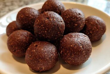 A close-up of several rich, dark brown No-Bake Brownie Batter Protein Balls stacked on a white plate.