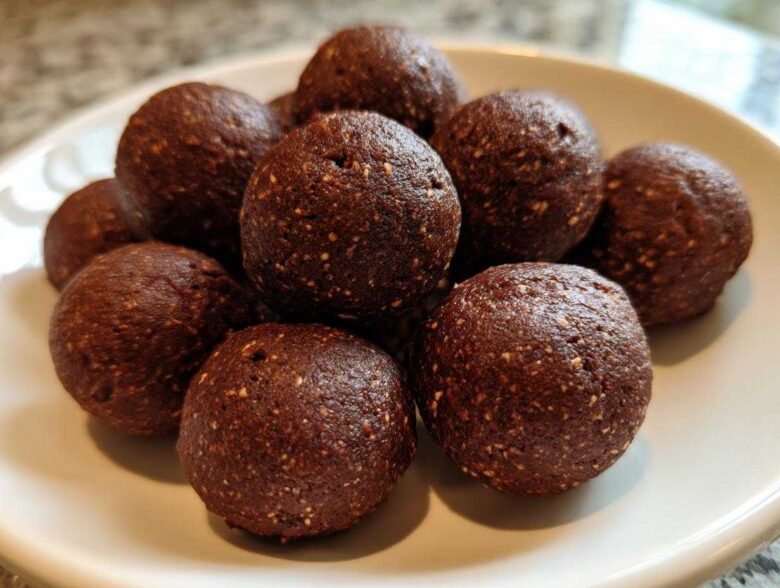 A close-up of several rich, dark brown No-Bake Brownie Batter Protein Balls stacked on a white plate.