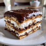 A decadent slice of No-Bake Chocolate Eclair Cake showing layers of graham crackers, cream filling, and rich chocolate frosting.