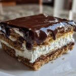 Close-up of a layered slice of No-Bake Chocolate Eclair Cake topped with dripping chocolate ganache.