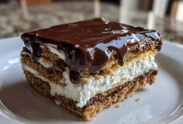Close-up of a layered slice of No-Bake Chocolate Eclair Cake topped with dripping chocolate ganache.