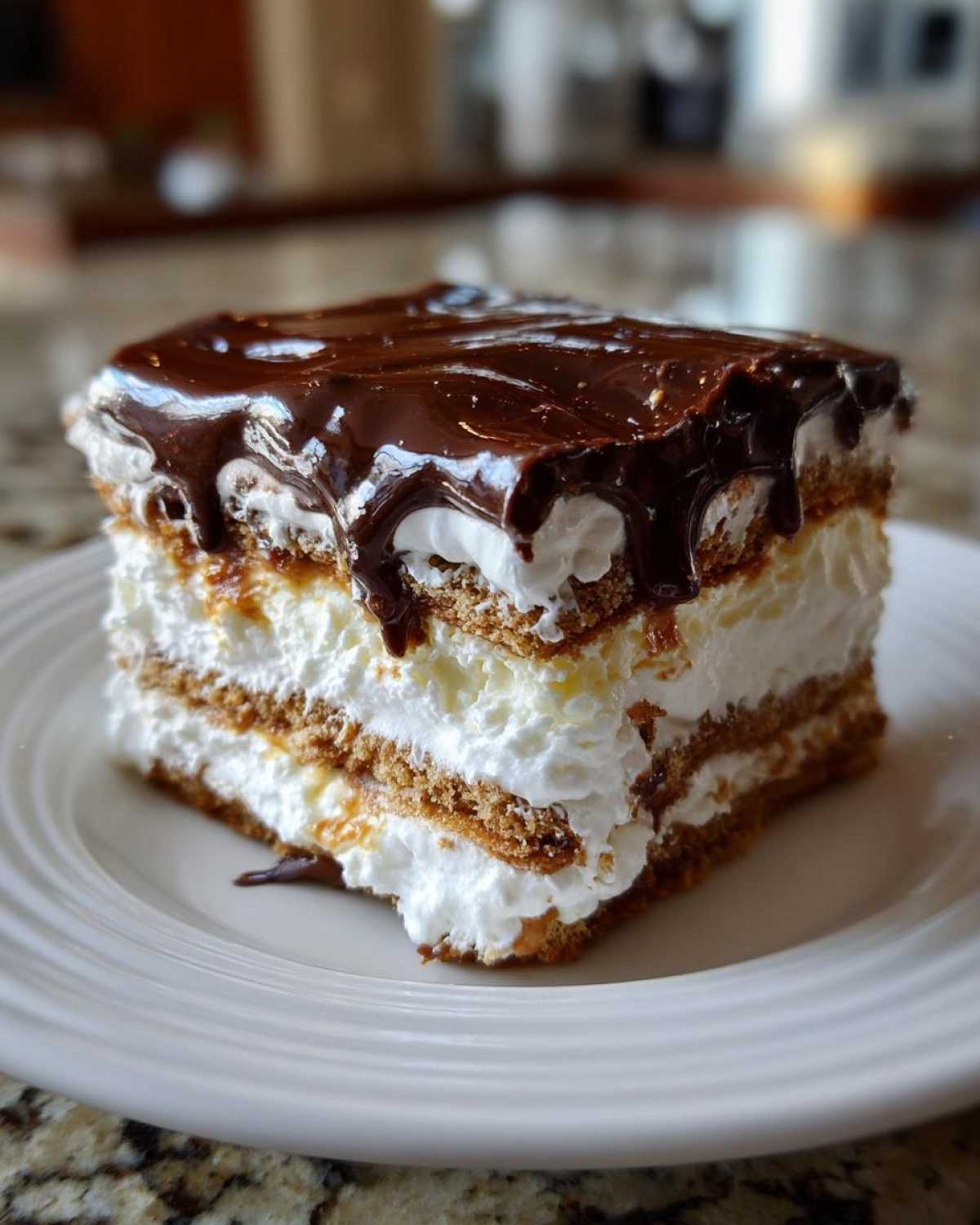 A tall, layered slice of No-Bake Chocolate Eclair Cake featuring graham crackers, whipped cream, and a rich chocolate glaze topping.