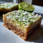 A close-up of a square No-Bake Coconut Lime Bars topped with shredded coconut and bright green lime zest.