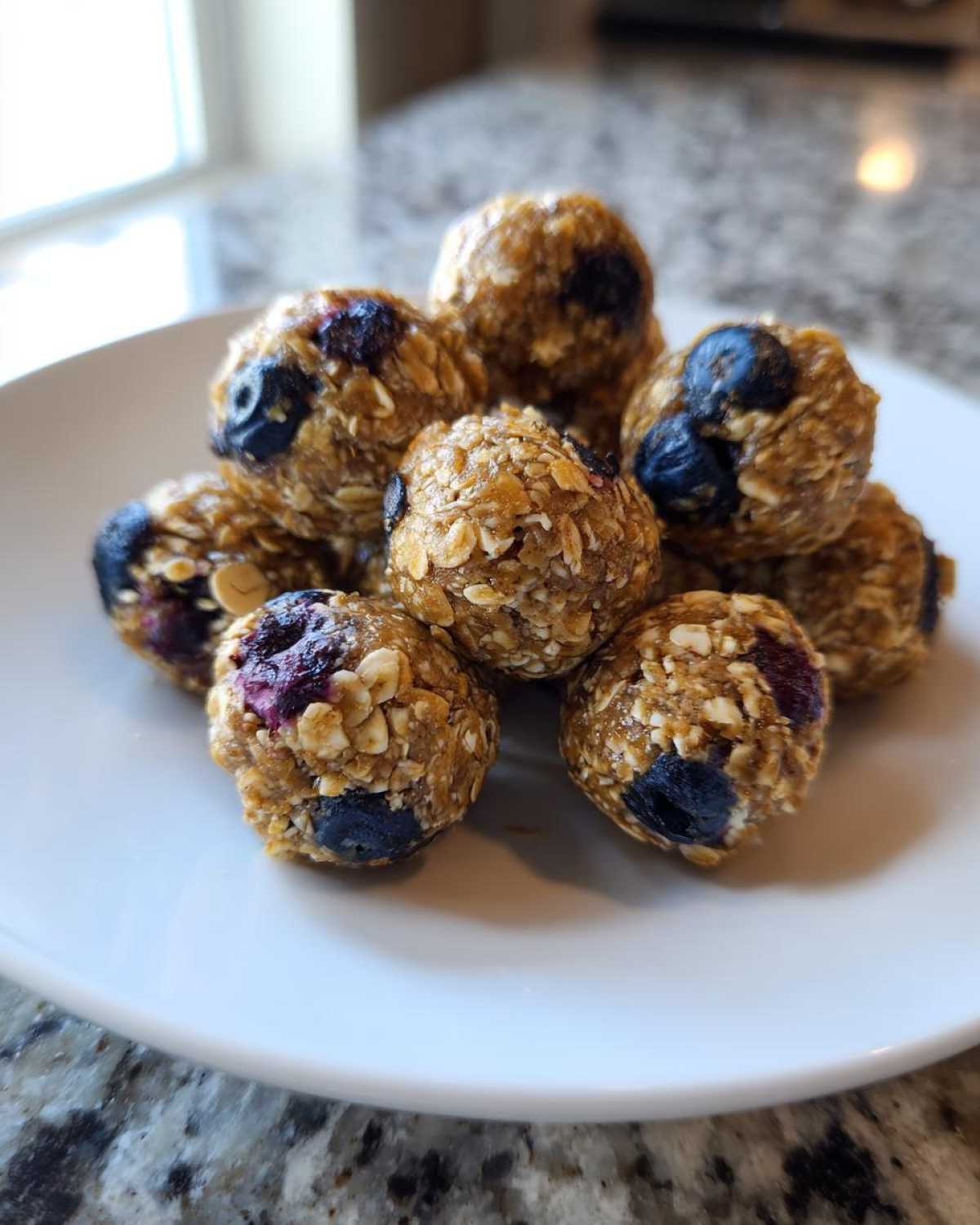 Close-up of several No-Bake Lemon Blueberry Energy Bites made with oats and visible blueberries on a white plate.
