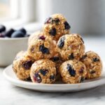 A stack of No-Bake Lemon Blueberry Energy Bites made with oats and dried fruit on a small white plate.