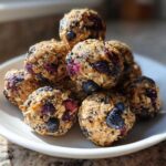 A stack of No-Bake Lemon Blueberry Energy Bites made with oats and visible blueberries on a white plate.