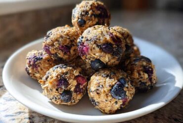 A stack of No-Bake Lemon Blueberry Energy Bites made with oats and visible blueberries on a white plate.