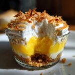 Close-up of a No-Bake Lemon Coconut Cream Pie Cup with a bite taken out, showing layers of crust, lemon filling, and toasted meringue.