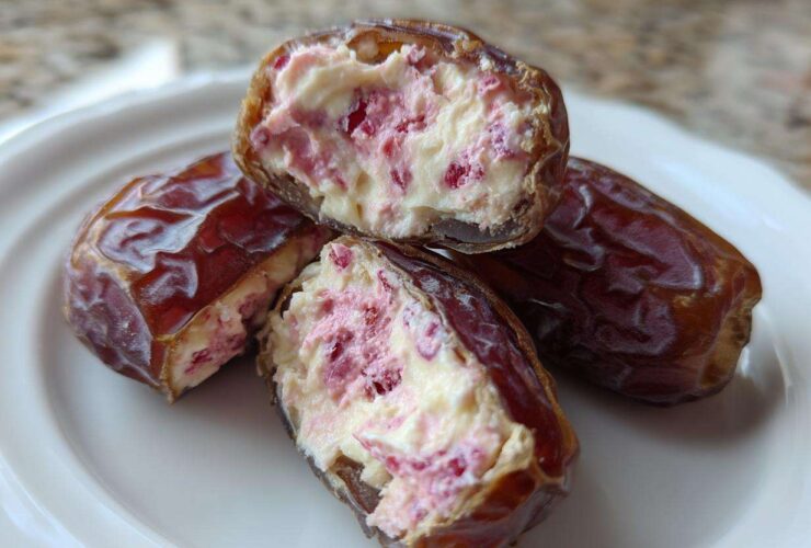 Close-up of No-Bake Strawberry Cheesecake Stuffed Dates cut open, revealing creamy filling with pink strawberry pieces.