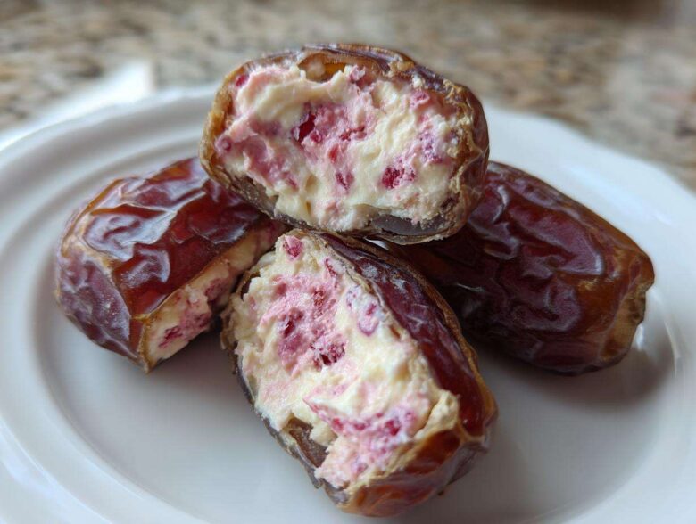 Close-up of No-Bake Strawberry Cheesecake Stuffed Dates cut open, revealing creamy filling with pink strawberry pieces.