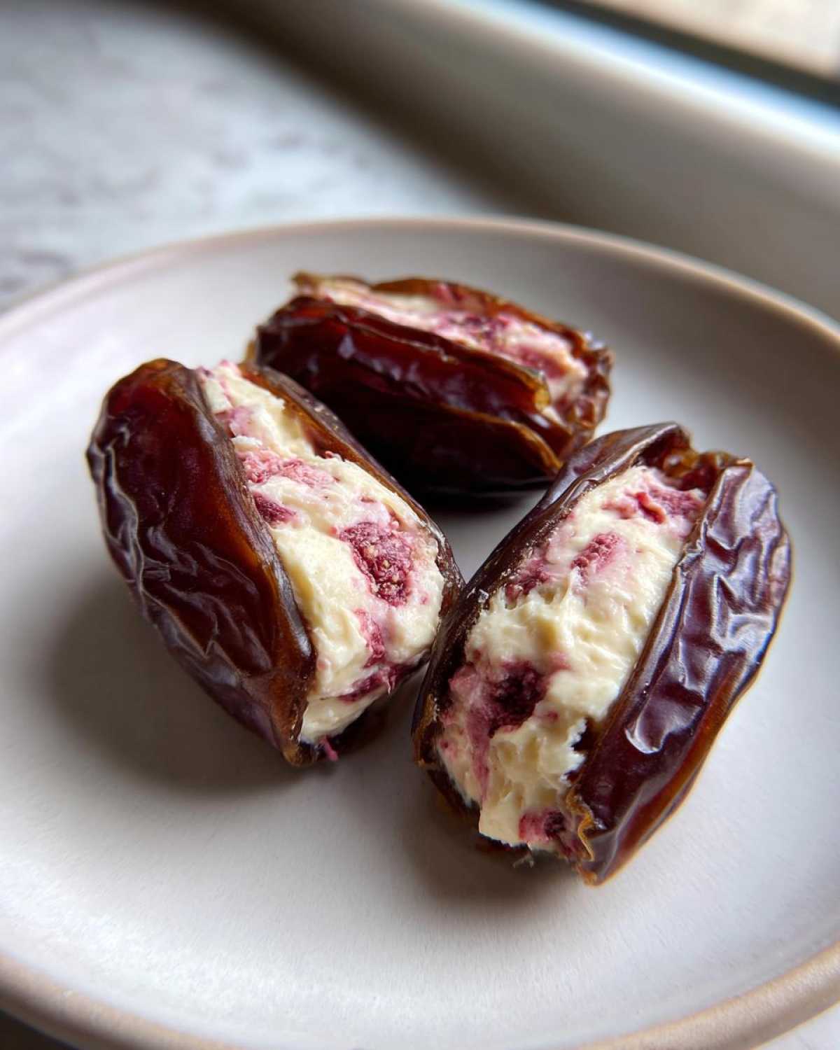 Three No-Bake Strawberry Cheesecake Stuffed Dates filled with creamy white and pink filling on a light plate.