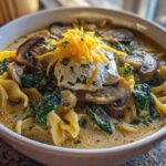 A close-up of One-Pot Creamy Spinach Mushroom Lasagna Soup topped with sour cream, shredded cheese, and mushrooms.