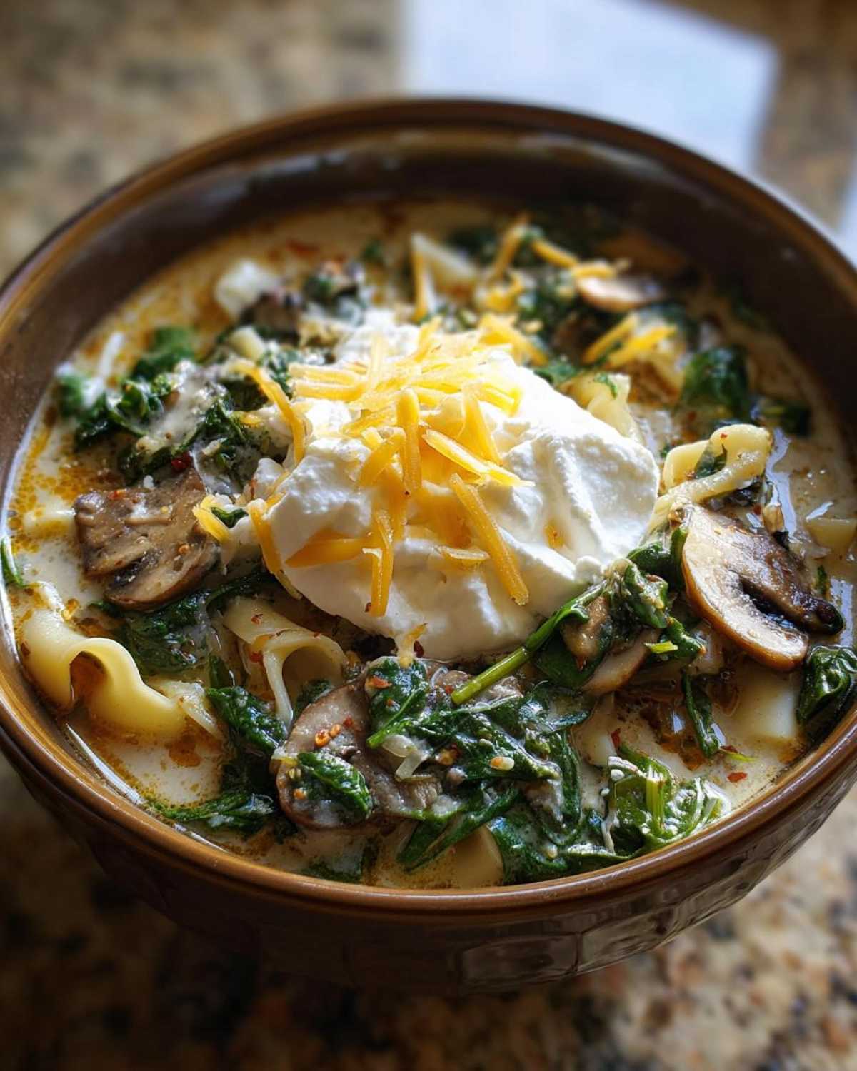 A close-up of One-Pot Creamy Spinach Mushroom Lasagna Soup topped with ricotta and shredded cheddar.