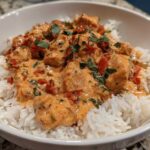 A close-up of One-Pot Creamy Tomato Basil Chicken and Rice served over fluffy white rice in a white bowl.